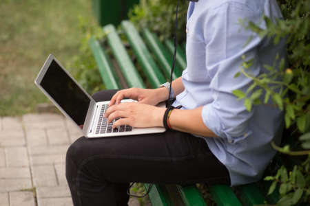 Closed up image of a student using a laptop and listening a music in headphone, sitting at on a...