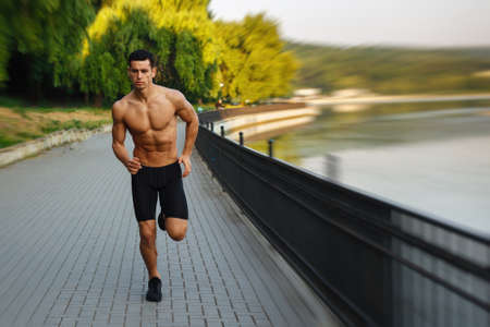 Image of a athlete young man with naked torso, Morning run in open air in urban park, early sunny summer morning. Sports lifestyle concept.の写真素材