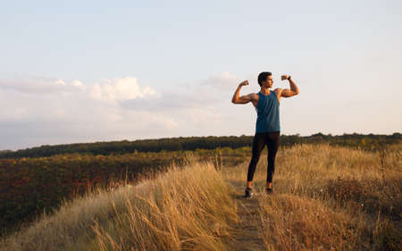 Back of a athlete, muscular, strong, fit, abs, sportive young man shows his muscles, isolated on a beautiful landscape background. Copy space.の写真素材