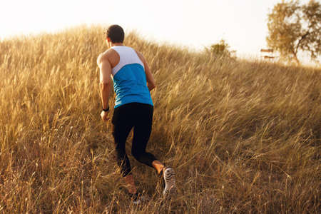 Back view of a strong, athlete, muscular, fit, sexy runner man in sportswear outside in the field, isolated on a beautiful sunset landscape background. Copy space.の写真素材