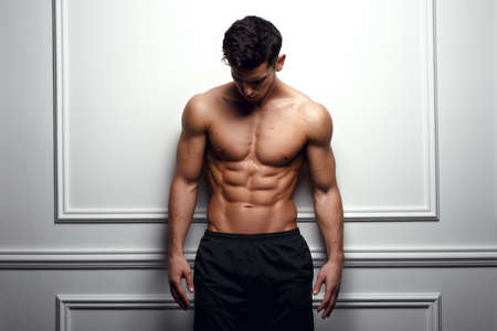 Stylish shirtless man at the white wall looking down, Horizontal studio shot.の写真素材