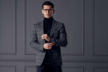 A handsome man in a gray jacket and black turtleneck, standing in front and looking confident, on gray wall background.の写真素材