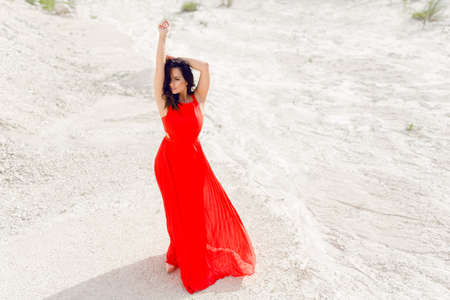 Young woman with hands up wearing the bright red dress. Horizontal outdoors shot.の写真素材