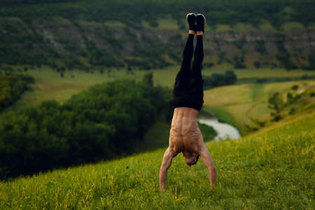 Muscular shirtless fit young man stand upside showing six pack abs on forest landscape background. Horizontal view.の写真素材
