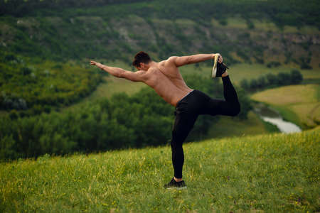 Athlete, muscular, fit, abs, young man doing stretching exercises before workout outside on forest, river background.の写真素材