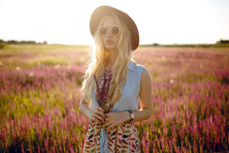 Beauty portrait of a sexy blonde with round floral eyeglasses, big lips,wavy hair and burgundy hat, looking at camera.の写真素材
