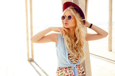 Sexy blonde girl with round sunglasses,denim shirt,cute dress,wave hair and burgundy hat ,enjoy the sunlight at sea.Horizontal view.の写真素材
