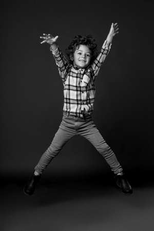 Frontal portrait of a jumping boy with to the side his arms and legs, shows his joy, happiness kid concept, freedom. Black and white image. isolated on a black background.の写真素材