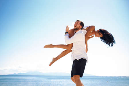 Two married young adults, men holding his wife passionately, sitting in the water, sunny day in...