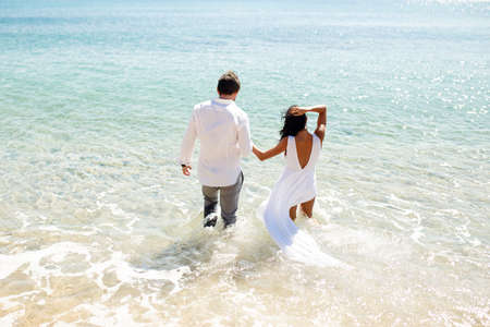 Back view of two young person newlyweds enter in water in clothing, enjoy in holiday, summer time, sea in Greece.の写真素材