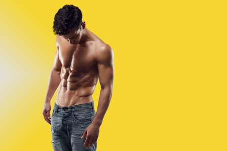 Torso of strong man in jeans posing in studio against light yellow background. Horizontal view.