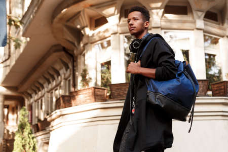 Guy on street, poses with attitude, with backpack on shoulder, looking a side, isolated on buildings...