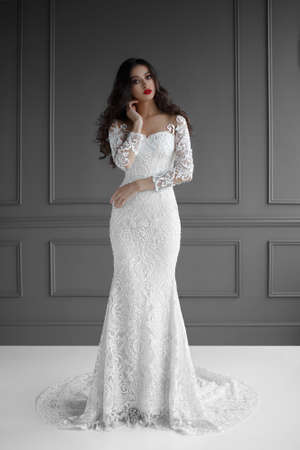 Wedding dress. Young Gentle Sensual Bride In Classic White dress. Looking at camera, isolated on a gray neoclassical wall. Girl with evening amazing make-upの写真素材