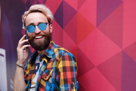 Close up portrait of happy hipster guy talking on cell phone and smiling, isolated on a colorful...