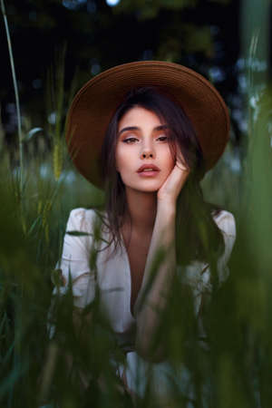 Beautiful Young Woman seated in the field in green grass, looking at camera with attitudine. Outdoors. Enjoy Nature. Healthy look girl on spring lawn. Allergy free concept. Freedom.の写真素材