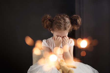 Frontal portrait of a unhappy little crying curly girl. Sad birthday, isolated on a dark background. Parent concept.の写真素材