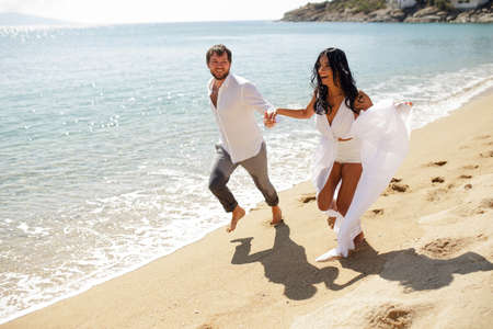 Happy couple just married young adults, men holding his wife passionately, running in the water, isolated on a seascape background.の写真素材