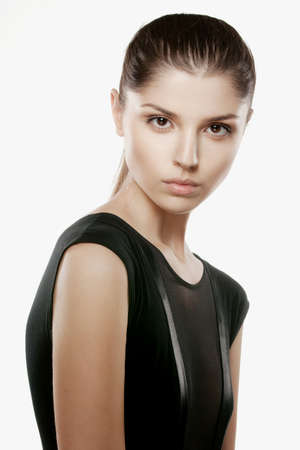 Beauty portrait of a tender brunette female model in elegant black dress, with tight hair, posing fashionable, over white background, shot in studio.の写真素材
