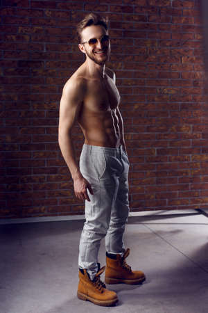 Full length isolated studio portrait of a young handsome man in white jeans and grey cardigan and boots. The stylish bearded guy posing over the concrete background, looking at camera.の写真素材