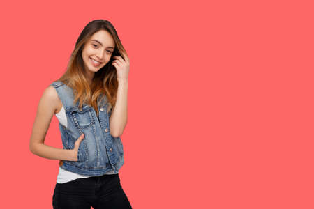 Hipster young woman in denim waistcoat, standing and looking at camera isolated over coral background. Copy space.の写真素材