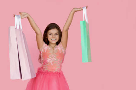 Portrait of a smiling teen in beautiful pink dress, holding shopping bags over pink background.の写真素材