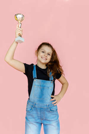 Happy little girl, smiling, showing a successful gesture of a winner, holding in hand a prize, over pink background.の写真素材