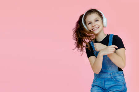 Portrait of a cute modern denim, girl teenager in denmwith headphones over pink background. Studio shot. Dance, motion image. Horizontal view, with space for text.の写真素材