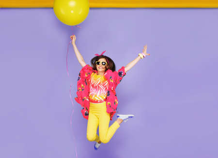 Smiling girl in sunglasses, jumping, holdiing a big balloons, isolated on violet background. Space...