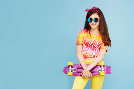 Portrait of an teen with sunglasses holding skateboard and looking at camera isolated on blue background. Copy space.の写真素材