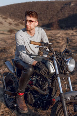 Handsome male in eyeglasses motorcyclist travels on motorbike, has adventure trip, likes active and admiring place.の写真素材