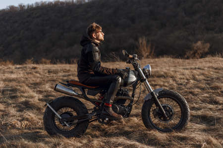 Male motorcyclist drives in nature on bike, wears black jacket, gloves, leather pants and boots, enjoys season, spends.の写真素材