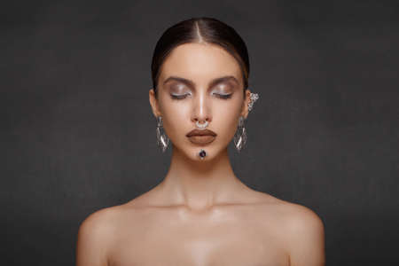 Beautiful girl with a jewelry on grey background, eyes closed. Frontal beauty portrait. Makeup,...
