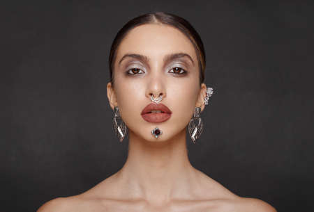 Gorgeous female model, with makeup jewelry, looking frontal at camera, posing in studio, isolated dark grey background.の写真素材