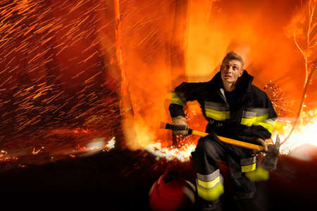 Equipped firefighter is in fire, life threatening, flames in forest space.