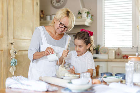 Cute little girl with her grandmother cooking together at kitchen table. Horizontal view.の写真素材
