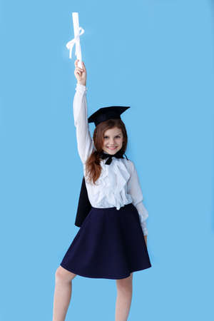 Happiness school girl in graduation cap standing over blue background and pointing away on empty space.の写真素材