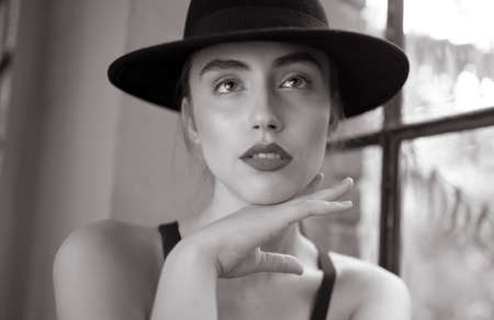 Horizontal view. Beauty portrait of a young woman with red lips, in black hat, sitting on chair,...