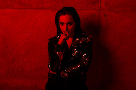 Girl with makeup and lips of black color, in the jacket, poses near concrete wall, holds his hand...