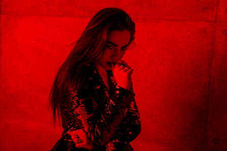 Seductive girl with makeup and lips of black color, in the jacket, poses in profile, holds his hand...