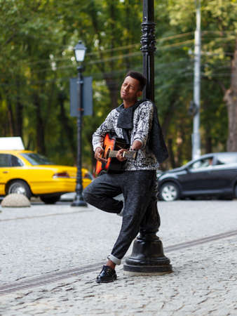 Young musician played on guitar, sing a song in sunny day, isolated on a blurred street background....
