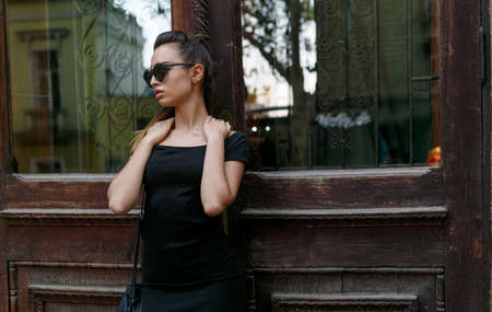 Profile portrait of a young girl hair gathered in a ponytail, posing outside in the street in black...
