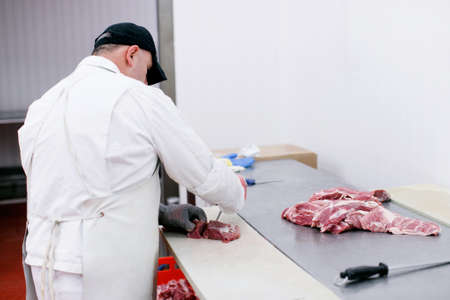 Anonymous worker in meat factory, chopped a fresh beef meat in pieces on metal work table, industry...