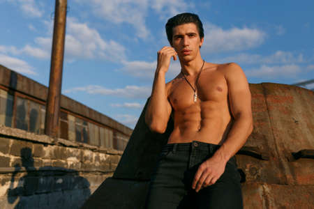 Handsome muscular and fit sportive young man with naked torso, dressed in black jeans, posing on old...