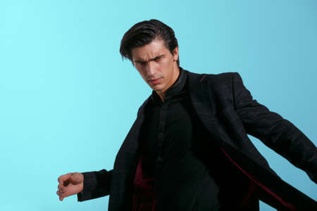 Portrait of attractive man in black suit, isolated on blue background. Horizontal view.