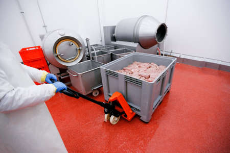 Frame image of a worker at a meat processing factory, pulls a load on which are crates of raw spicy meat. Process for the production of products of animal origin.の写真素材