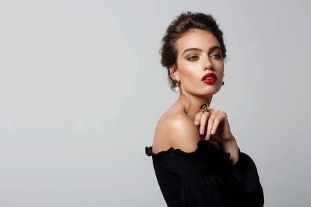 Portrait of a woman in with makeup, red lipstick in elegant black dress with naked shoulders, wears luxury stone jewellery, over white background. Space for text.の写真素材