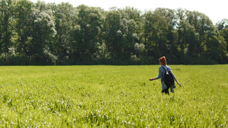 Freedom and liberty concept with copy space. Unrecognizable lonely girl with red hair walking on summer meadow. Rear view.の写真素材