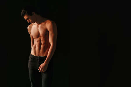 Strong athletic handsome man with naked torso, showing his six abs on dark black