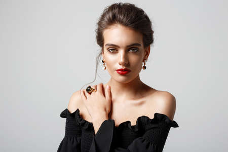 Frontal portrait of a gorgeous woman in elegant black, wears luxury stone jewellery, over white...