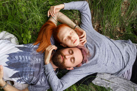Closeup portrait of a couple, seated down on a green grass, seated down with turned heads with closed eyes.の写真素材